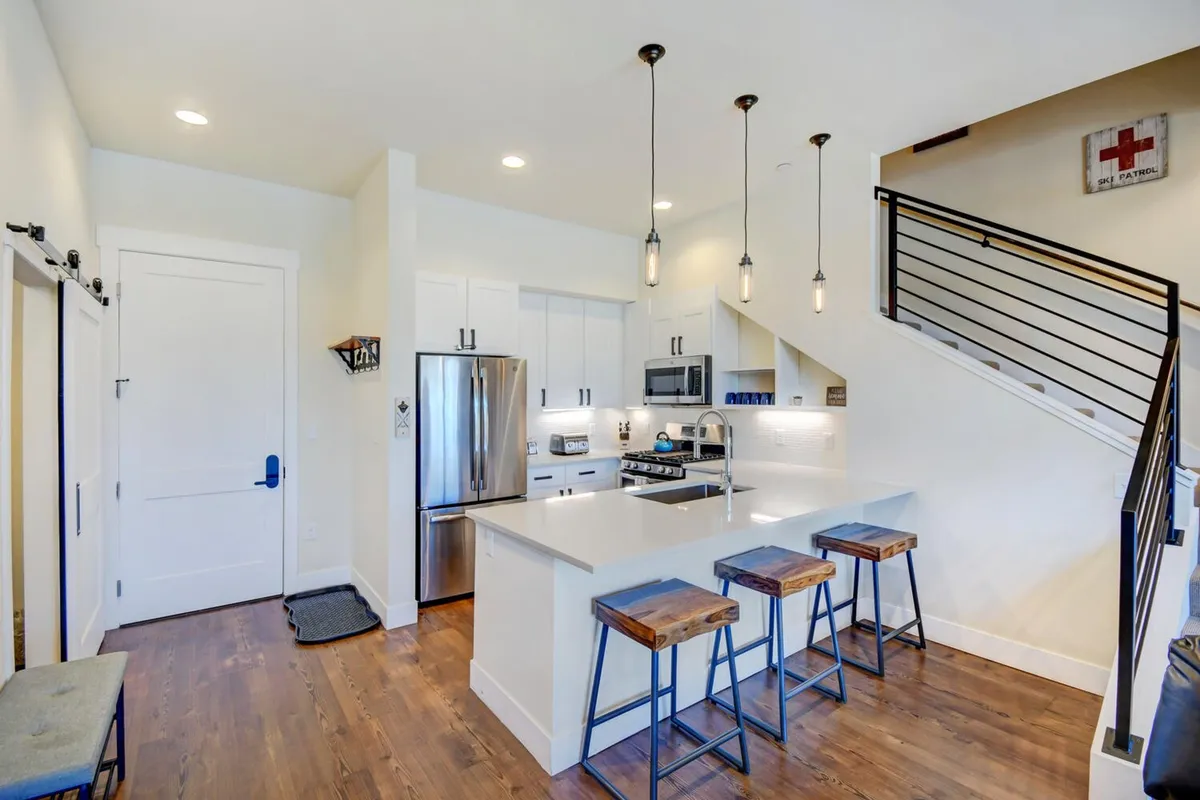 A spacious, upscale kitchen featuring a large island with stools, stainless steel appliances, and elegant pendant lights. The scene is inviting and suggests both casual family meals and more formal entertaining.