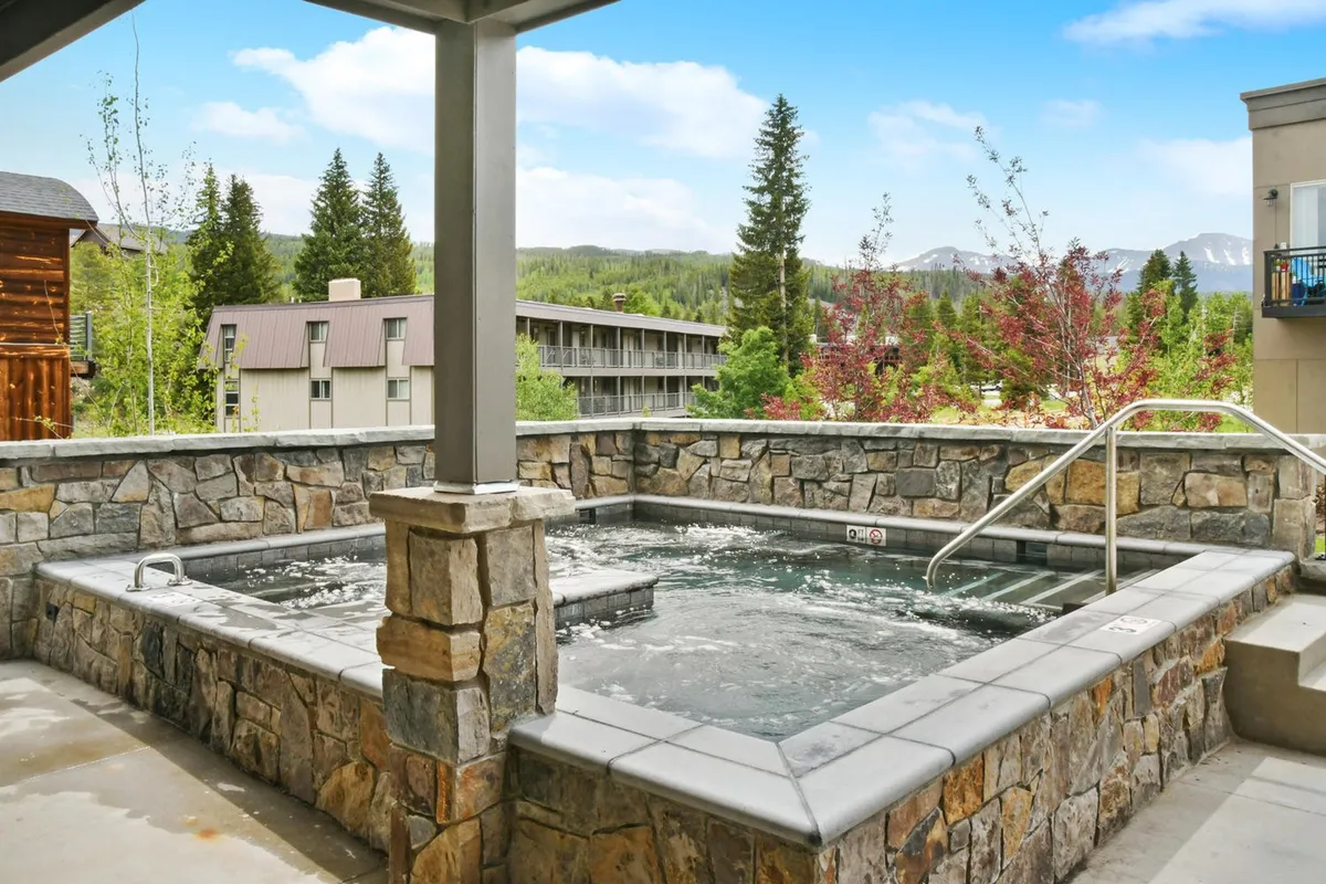 This exterior image showcases a tranquil hot tub set amidst natural surroundings with mountain views. The mood is calm and inviting, perfect for relaxing and socializing while enjoying the scenery. The hot tub is large, suggesting ample space for multiple guests.