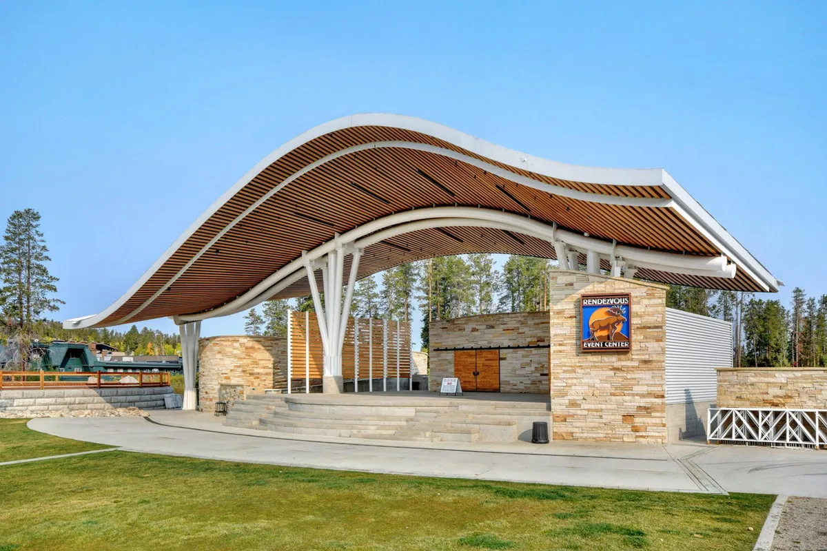 This exterior image captures the distinctive curved roof and stone walls of what appears to be an amphitheater, with a staircase leading up to the stage. The scene is set outdoors and suggests a lively, communal venue ideal for concerts and gatherings.