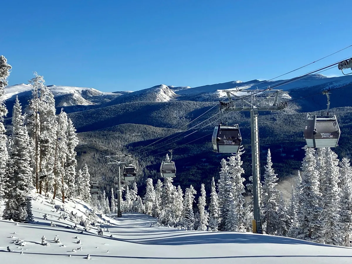 A sweeping mountain landscape featuring snow-covered trees, a ski lift ascending the slope, and expansive mountain ranges in the background. The image evokes a sense of adventure and the natural grandeur of the area, perfect for skiing, snowboarding, and photography enthusiasts.