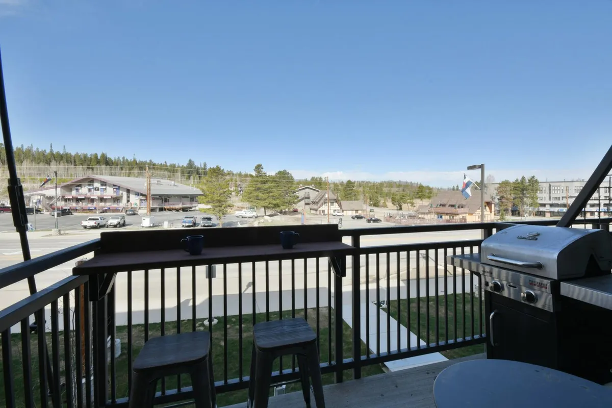 This image features an outdoor grill, bar stools, and a view of the surrounding area—likely from a private balcony or terrace. The setup evokes a relaxed atmosphere ideal for al fresco dining or enjoying a morning coffee while soaking in scenic views.