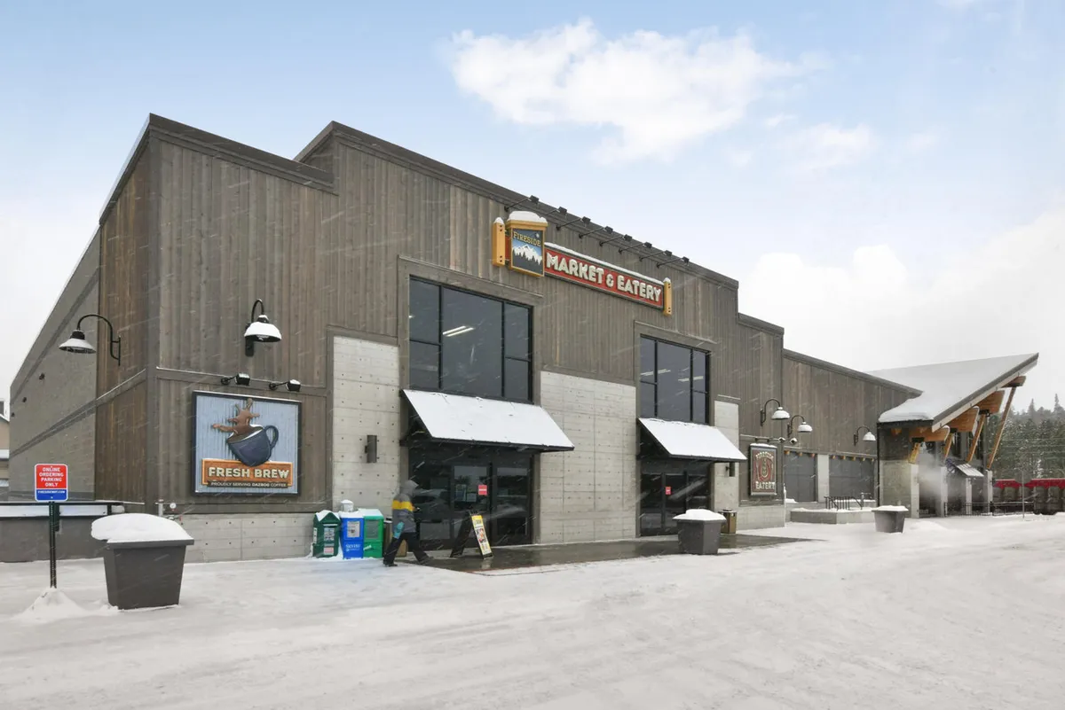 The entrance to Fireside Market is showcased with prominent signage, snow-dusted ground, and an inviting outdoor seating area, hinting at the ease of grocery shopping and casual community gatherings. The scene feels welcoming and central to daily family life.