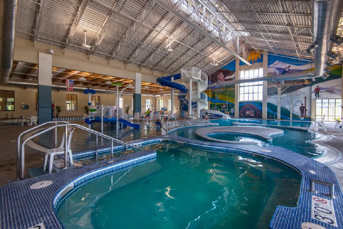 A lively indoor pool scene featuring children joyfully playing on water slides and families gathered around the pool. The space is filled with energetic movement and vibrant colors, creating a sense of fun and adventure.