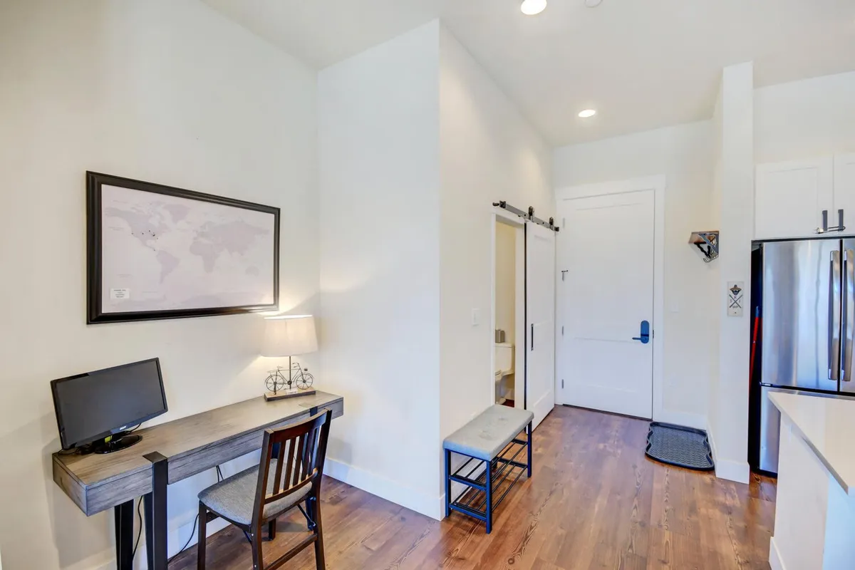 A contemporary open-plan interior with a desk and computer, map-themed artwork, comfortable bench seating, and a kitchen area. The space evokes relaxation, productivity, and social interaction, with hints of modern exploration and planning.